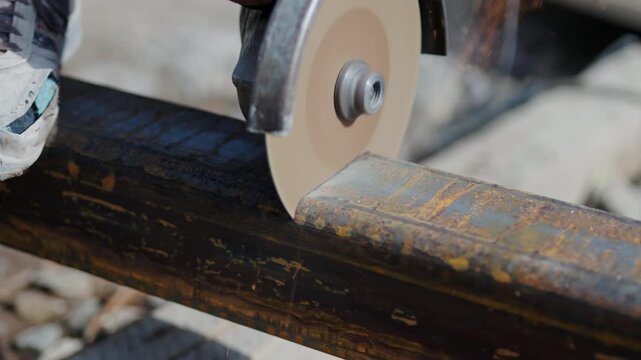 Worker cuts hollow structural section with circular saw at construction site closeup. Laborer works with metal beam and manual tool