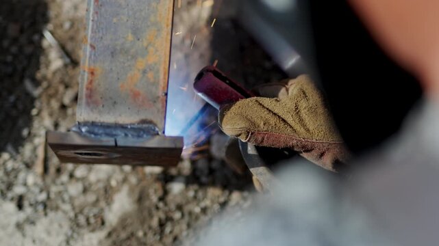 Laborer in protective gloves welds metal carcass at construction site closeup. Skilled welder attaches steel beams with heat upper view