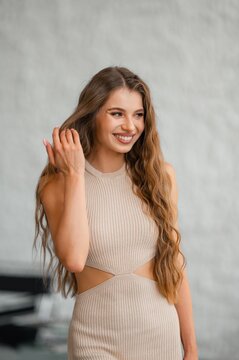 Smiling brunette woman in beige ribbed knit top with long wavy hair in neutral gray studio portrait