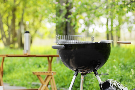 Modern brazier with grate near folding table in forest