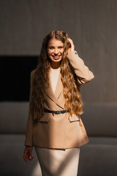 Smiling woman wearing beige blazer standing outdoors under bright sunlight showcasing warm neutral tones, long wavy hair, confident pose, fashion portrait for lifestyle and fashion campaigns