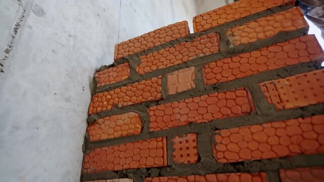 Builder hand removes excessive concrete mix from brickwork with mortar closeup. Worker makes wall inside building at bricklaying slow motion