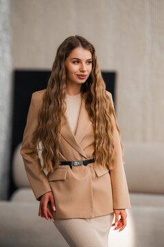 Elegant woman in beige blazer and matching coat with long wavy hair stands outdoors in urban setting, exuding confident chic style for modern lifestyle editorial portrait