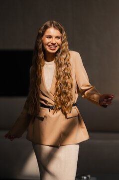 Smiling woman wearing beige blazer over knit top with long wavy hair in studio portrait under warm lighting, showcasing fashion model style, elegant casual look for editorial use