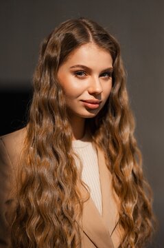 Closeup studio portrait of brunette woman with long wavy hair wearing beige blazer over cream knit top under soft warm lighting and calm gaze