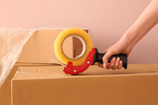 Moving and relocation logistics, person using tape dispenser to seal cardboard box for shipping or storage preparation in a home or warehouse setting