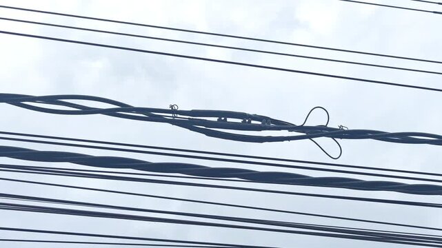 Pan right video of a completed joint on twisted aerial cables, industrial electrical power grid and overhead distribution network infrastructure against a cloudy sky.