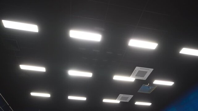 Modern led lighting equipment glows on ceiling in reconstructed cinema hall bottom view. Energy efficient lamps give illumination in office