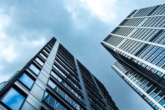 Low angle view of modern skyscrapers with blue windows against cloudy sky showing urban architecture height perspective and business scale