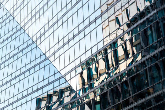 Glass building facade with reflections of neighboring architecture creating an abstract grid pattern of windows lines and urban geometry