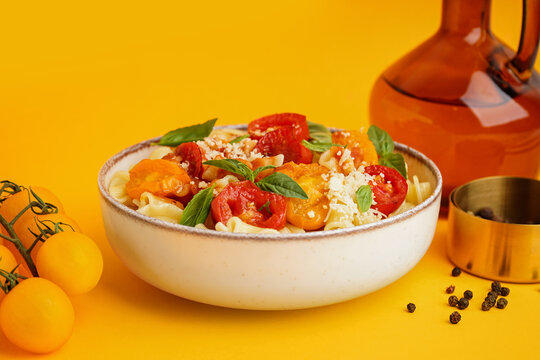 Bowl of tasty pasta with tomato and basil on yellow background