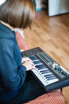 Woman playing electronic keyboard synthesizer at home in casual wear, music creation