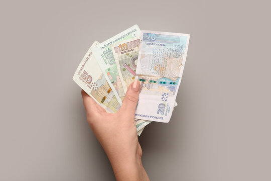 Female hand holding Bulgarian lev banknotes on grey background