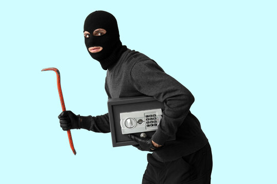 Male thief with crowbar and safe box on blue background