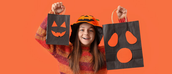 Obraz premium Halloween celebration and trick or treat, happy girl holding paper bags with spooky faces and wearing pumpkin hat on a bright orange background