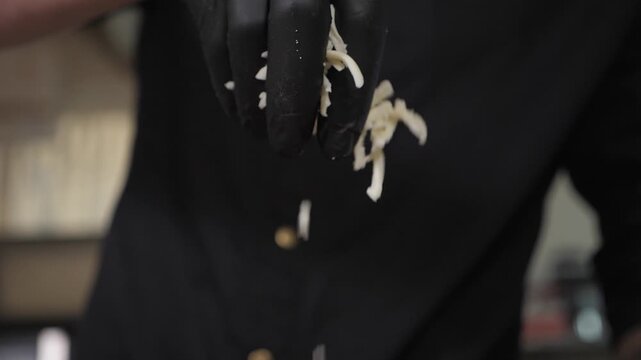 A close-up of a chef in gloves holding grated cheese in his hands and slowly sprinkling it onto the pizza. The process of making pizza at a fast food restaurant.