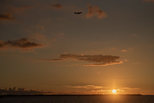 オレンジ色の夕暮れの空を飛ぶ飛行機とシルエットの防波堤