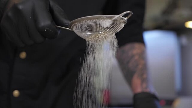 Close-up of a male chef sifting flour through a sieve in the kitchen of a restaurant. The process of making pizza dough in a pizzeria is shown.