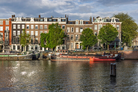 Amsterdam, Netherlands: Row of historic Dutch canal houses and houseboats along the Amstel river, capturing authentic local architecture and urban lifestyle.
