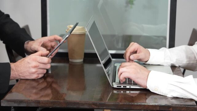 A businessman's hands are typing on a laptop and writing code at a coffee shop. The concept is to work from anywhere.