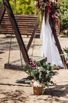 Photo of basket with fresh colorful flowers against wooden swing in outdoor park.