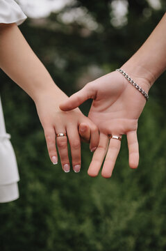 Close-up wedding photo of newlyweds, bride and groom holding hands outdoors.