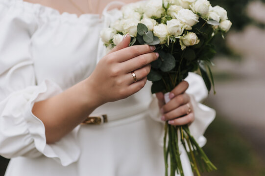 A close-up wedding photo of a bride holding a bouquet of flowers in her hand with a gold ring on her finger.