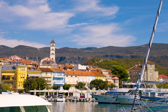 Scenic waterfront view of Crikvenica with colorful Mediterranean houses, the church tower, marina boats, and forested mountains rising behind the town