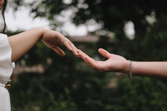 Close-up wedding photo of newlyweds, bride and groom, touching hands, fingers to each other in the open air.