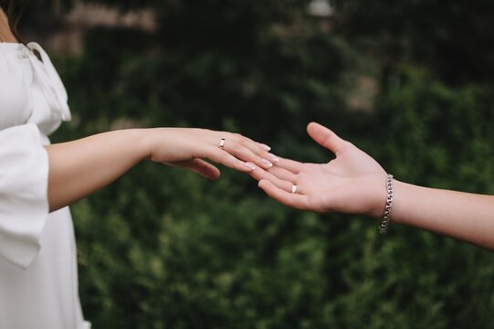 Close-up wedding photo of newlyweds, bride and groom, touching hands, fingers to each other in the open air.