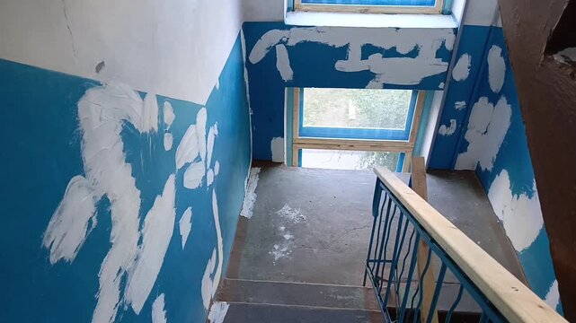 Plastered holes and repaired wall damage on a stair landing inside a residential building, representing entrance renovation, wall leveling, plastering and repair work.