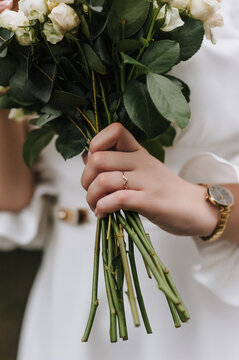 A close-up photo of a bride holding a bouquet of flowers in her hand with a gold ring on her finger.
