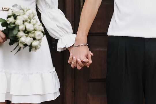 Close-up wedding photo of newlyweds, bride and groom holding hands.