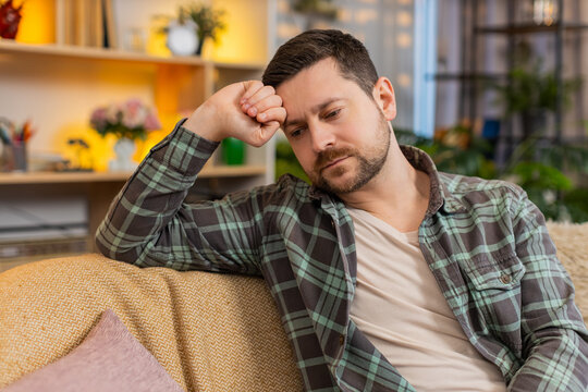 Young man on home sofa falls asleep from exhaustion with closed eyes and tired pose after stress routine. Adult guy on home sofa drifts into rest in living room while coping with fatigue and burnout.