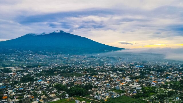 Aerial view of Mount Salak towering over the dense urban landscape and residential rooftops in Bogor City, West Java, Indonesia.