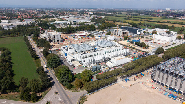 Aerial view of the Vantage VDC MXP2 data center construction site featuring large industrial buildings, cranes, and surrounding green fields in Castelletto, Lombardia, Italy.