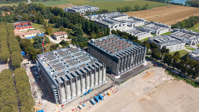 Aerial view of the DATA4 DC15 data center complex with large industrial buildings and rooftop cooling units, surrounded by trees and fields in Castelletto, Lombardia, Italy.