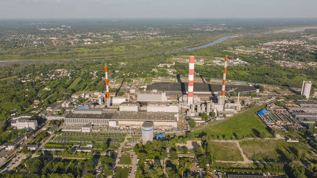 Aerial view of the Siekierki Power Station featuring tall striped chimneys, industrial buildings, and coal storage areas surrounded by green landscapes in Warsaw, Masovian Voivodeship, Poland.