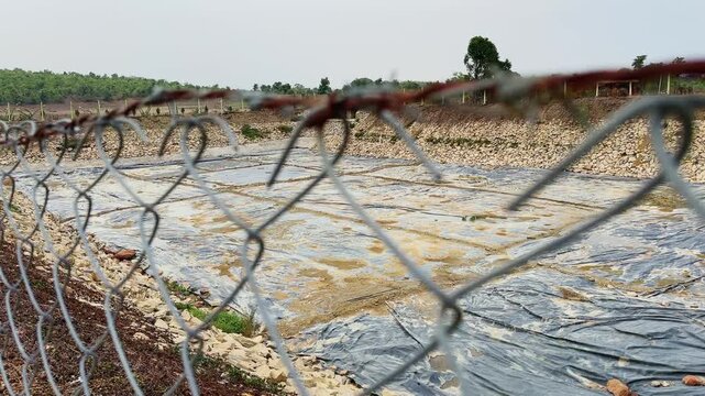Jib up view of a lined agricultural farm pond with HDPE geomembrane, stone pitched embankments and chain link fencing