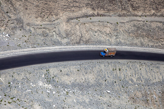 Aerial view of a colorful decorated truck driving along the winding Karakoram Highway through the rugged rocky terrain of the mountains in Ali Abad, Gilgit Baltistan, Pakistan.