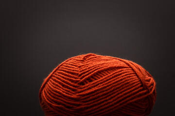 Red yarn ball with trailing thread and a crochet hook on a dark background, crochet supply.