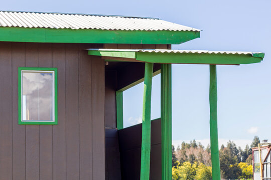 A close-up architectural detail of a brown wooden structure with bright green trim and a corrugated metal roof