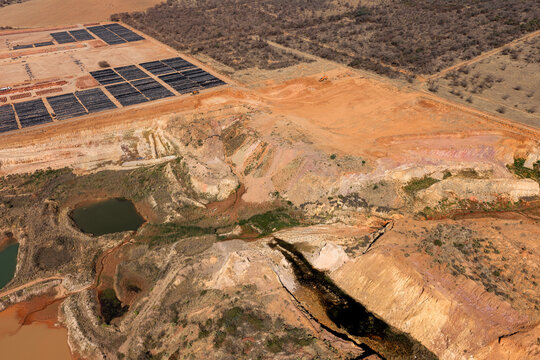 Aerial view of an open-pit clay mine showing excavation layers, water pools, and nearby brick manufacturing stacks in eMalahleni, Mpumalanga, South Africa.
