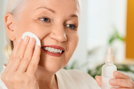 Healthy aging and skincare routine, mature woman applying facial serum with cotton pad for anti-aging treatment and skin wellness in a bright home