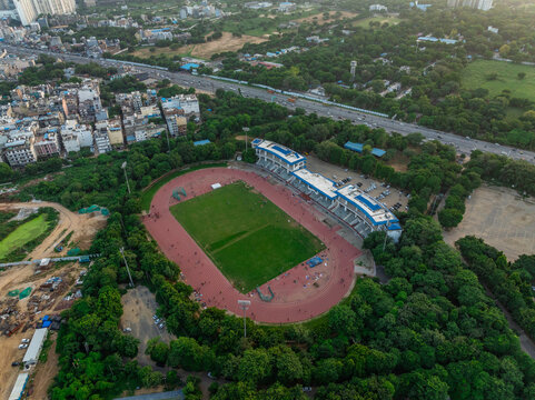 Aerial view of Tau Devi Lal Stadium with its running track and green field surrounded by dense trees and urban infrastructure in Gurgaon, Haryana, India.