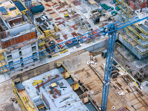 Aerial view of a large real estate construction site featuring a blue tower crane, concrete foundations, steel reinforcement bars, and building materials in Poland.