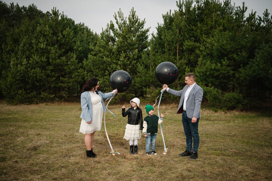 Happy family with two children holding black gender reveal balloons for twins outdoors in a pine forest.