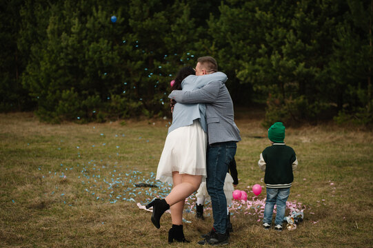Loving couple hugging each other tenderly with children nearby during a twin gender reveal celebration in a forest.