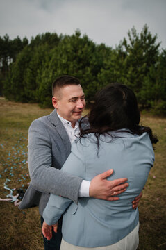 Loving husband embracing his pregnant wife tenderly outdoors in a forest during a twin gender reveal celebration.