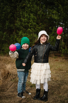 Cute little boy and girl holding small blue and pink balloons smiling outdoors in a forest during a family celebration.